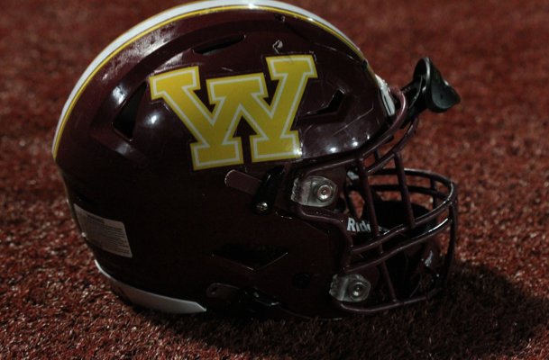 A varsity football player’s red-and-gold helmet glows underneath the stadium lights during the Homecoming game.